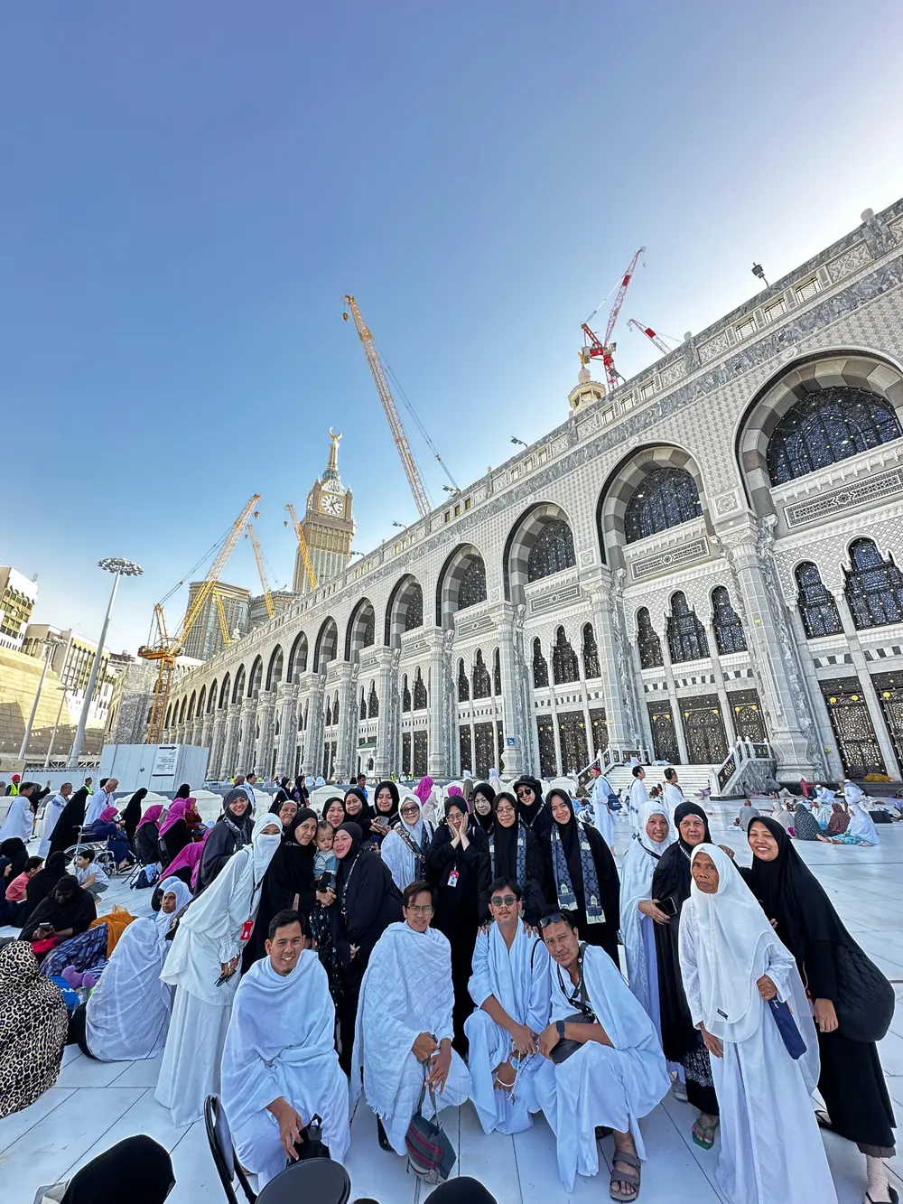 Jamaah berihram duduk di pelataran Masjidil Haram, menara jam Makkah di latar